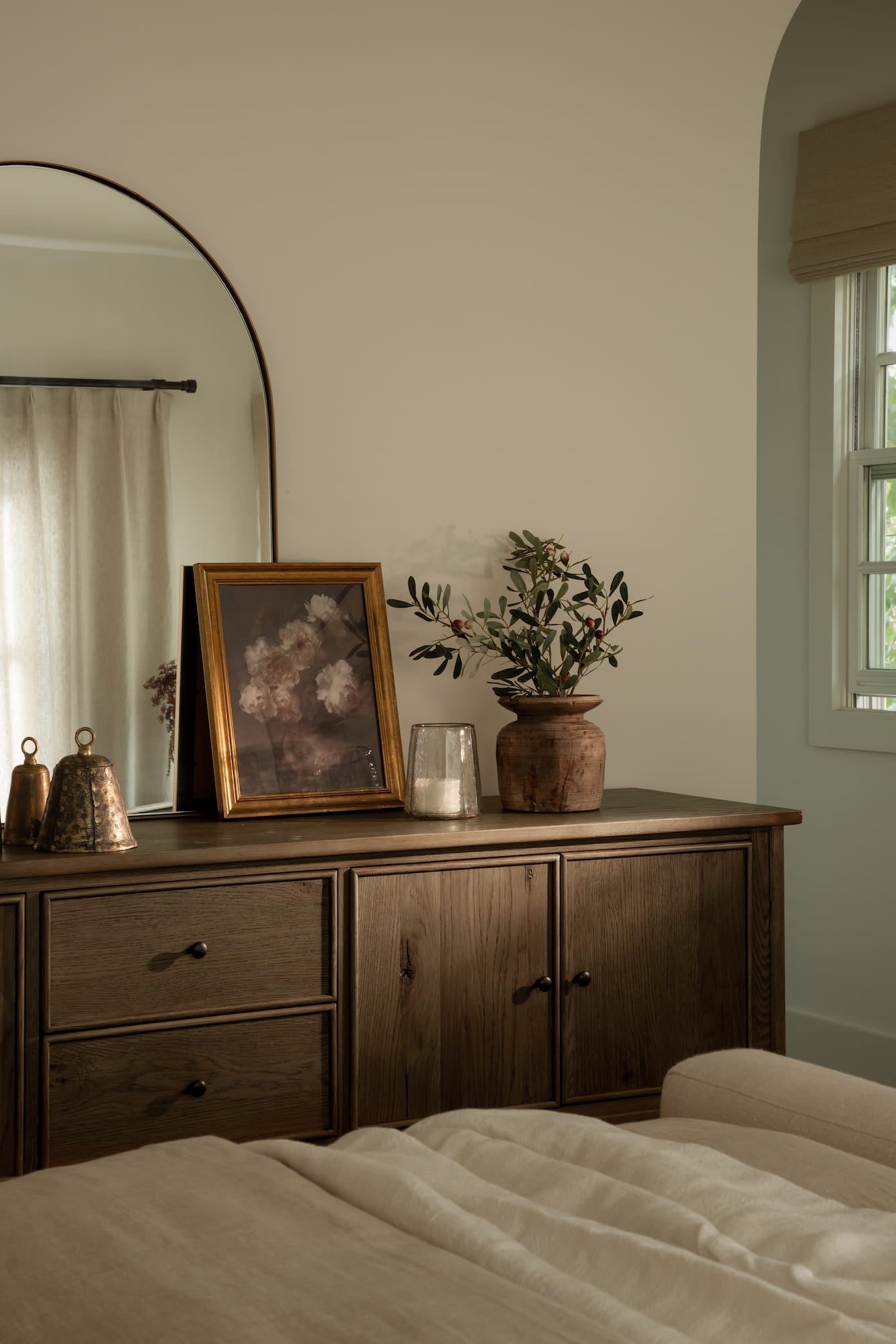 Soft neutral bedroom with upholstered bed, layered linen bedding, wood nightstands, and textured pendant light.