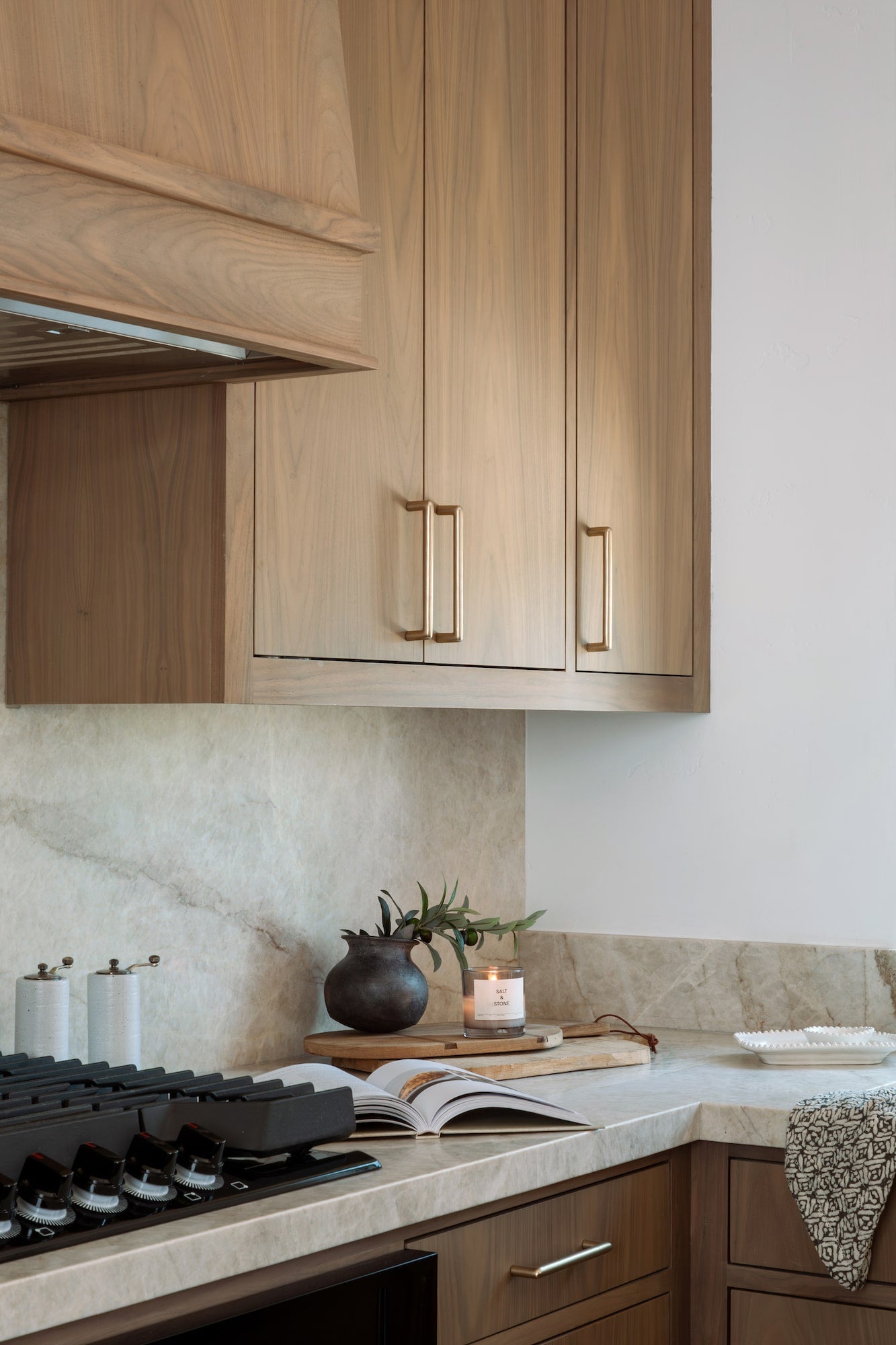 Close-up of wood upper cabinets with brass hardware above stone backsplash and countertop.