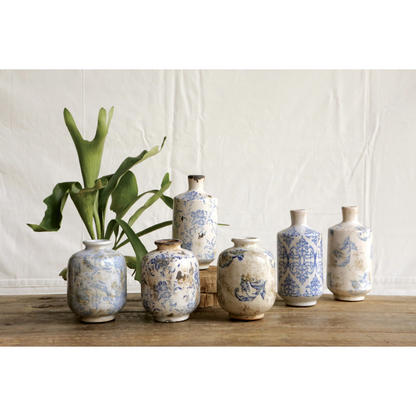 Small blue and cream patterned terra-cotta vases grouped on a wooden table with a green plant