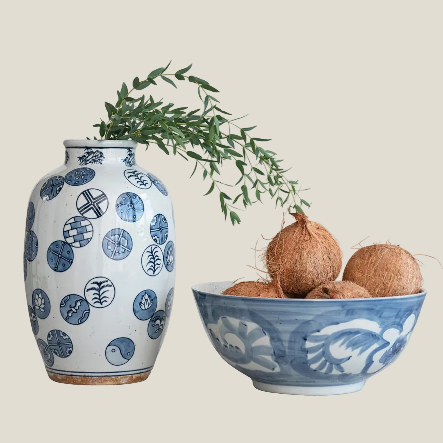 The Hampton Bloom Bowl with coconuts next to a blue and white vase holding a green branch, styled still life