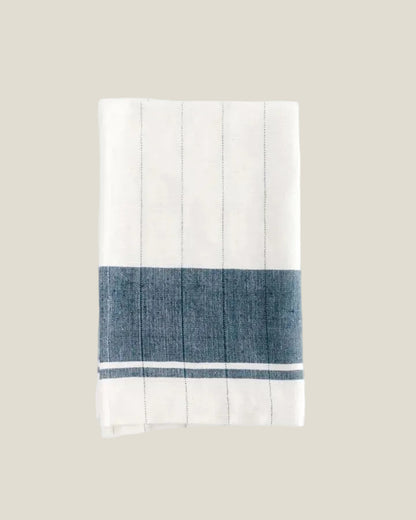 The Chelsea tea towel in ivory with fine pinstripes and a navy stripe band, shown folded from above