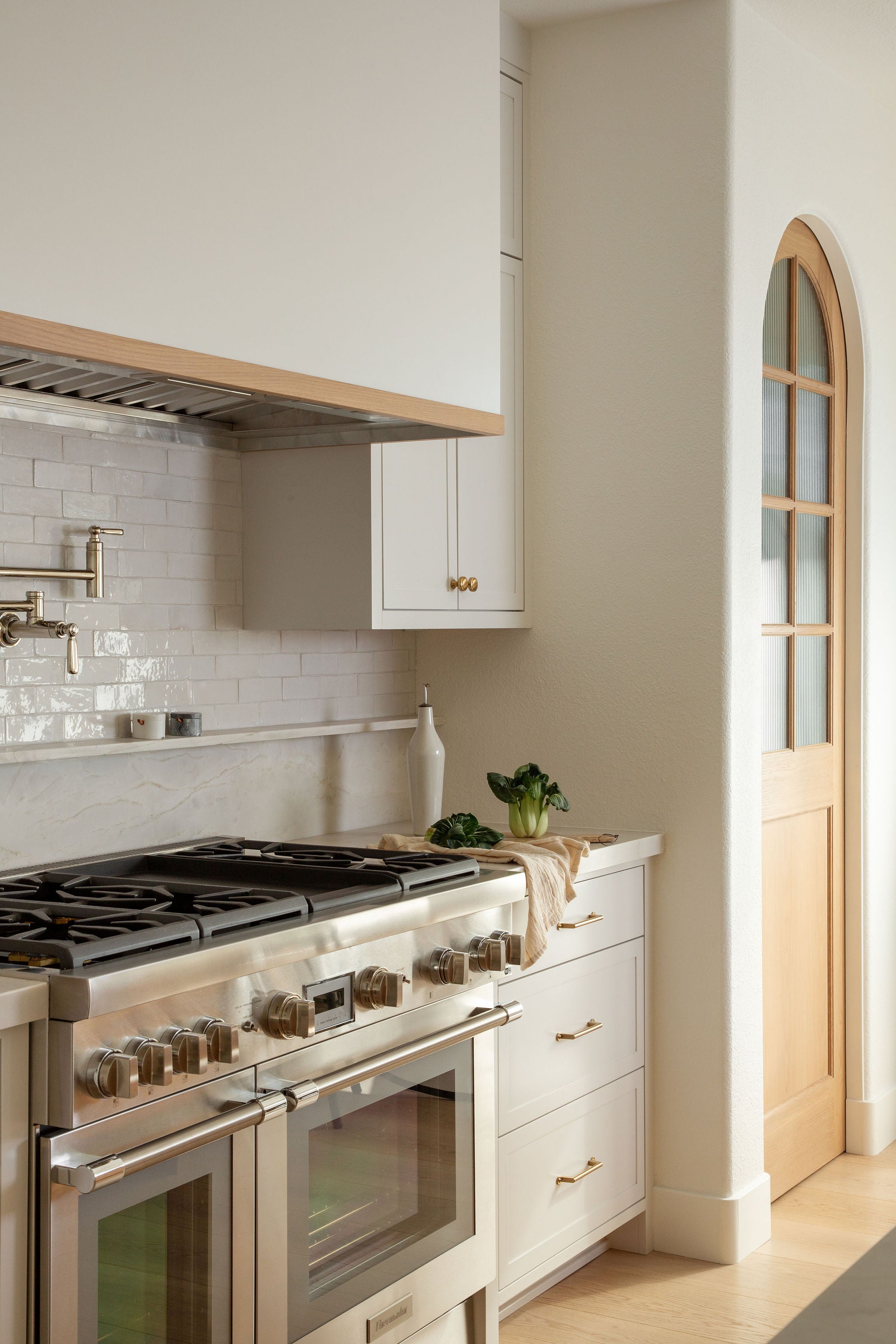 Mixed hardware finishes featuring the warm Atlas Bradbury pull alongside cooler pot filler, faucet, and stove finishes