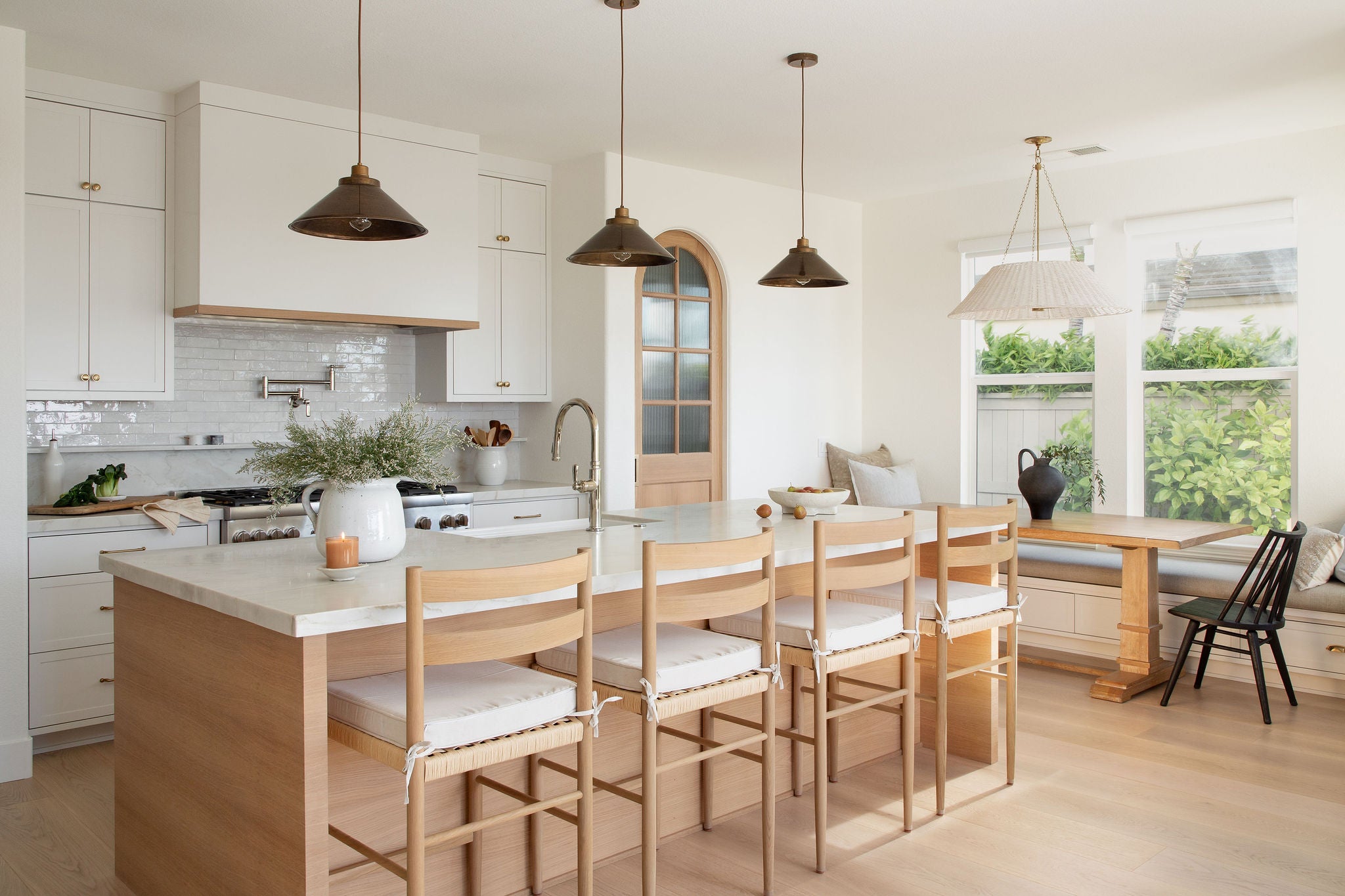 Modern kitchen with island and chairs, featuring white cabinets and a large window.
