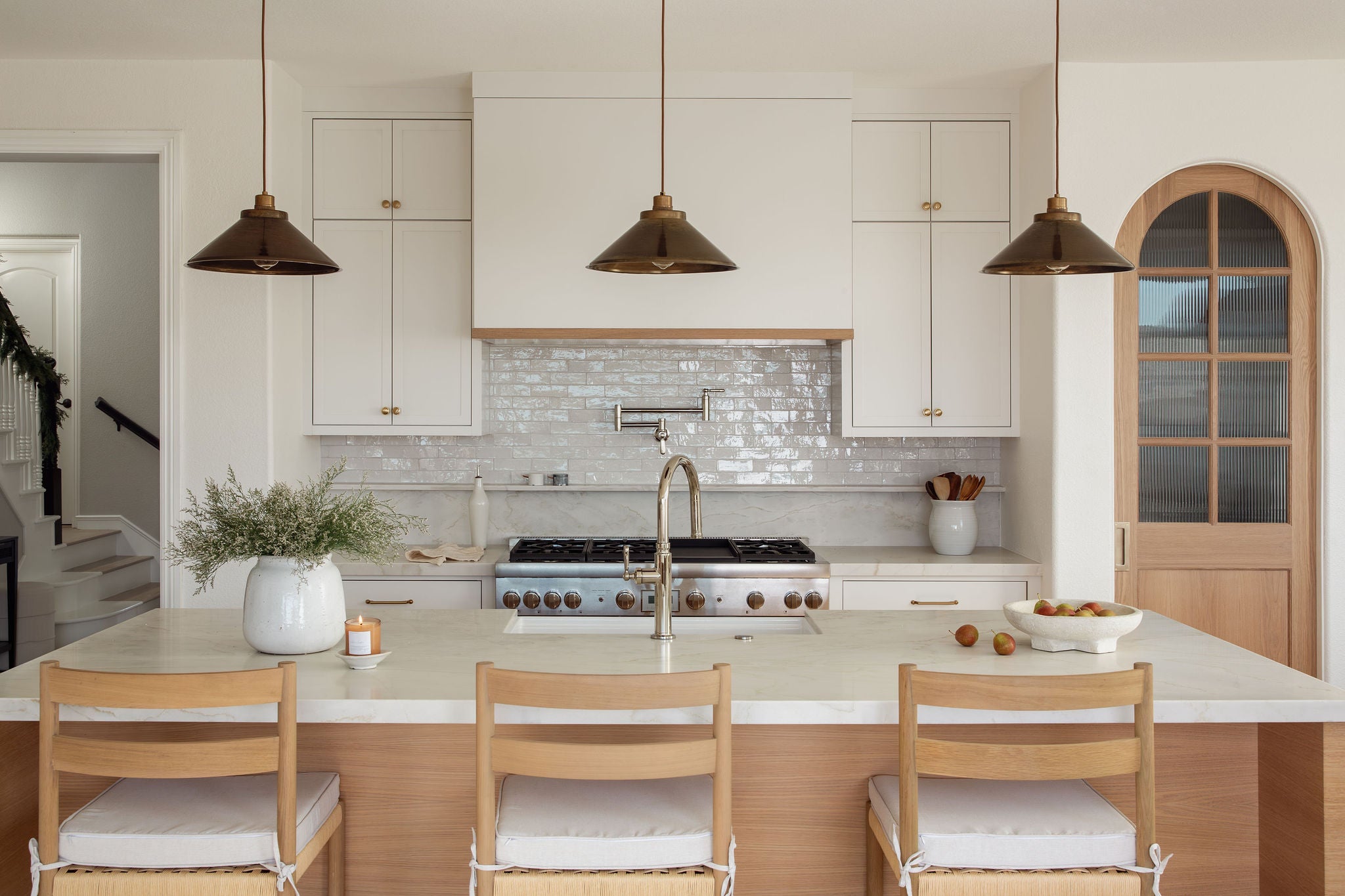 Modern kitchen with white countertops, wooden chairs, and stainless steel appliances.