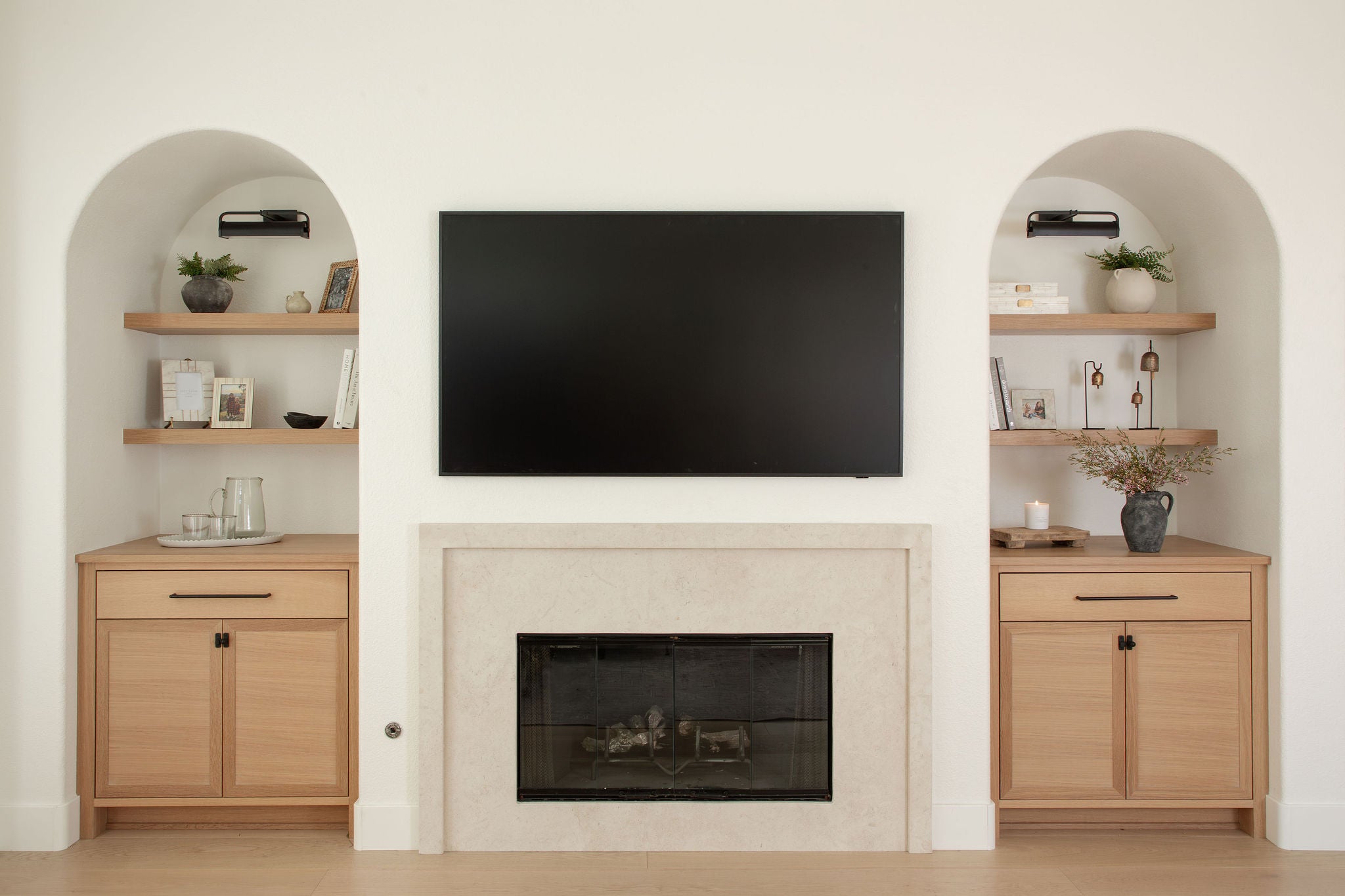 Modern living room with a television mounted above a fireplace, flanked by wooden cabinets and shelves.