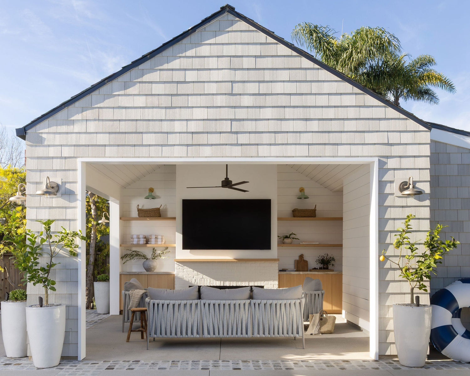Cedar shingle pool house with open-air outdoor living room, ceiling fan, and media wall at the Dover Shores whole-home renovation, Newport Beach, California — Joey Snow Design Co.