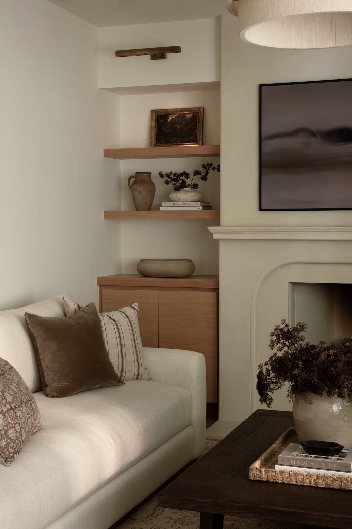 Floating wood shelves styled with pottery and artwork beside curved plaster fireplace surround.