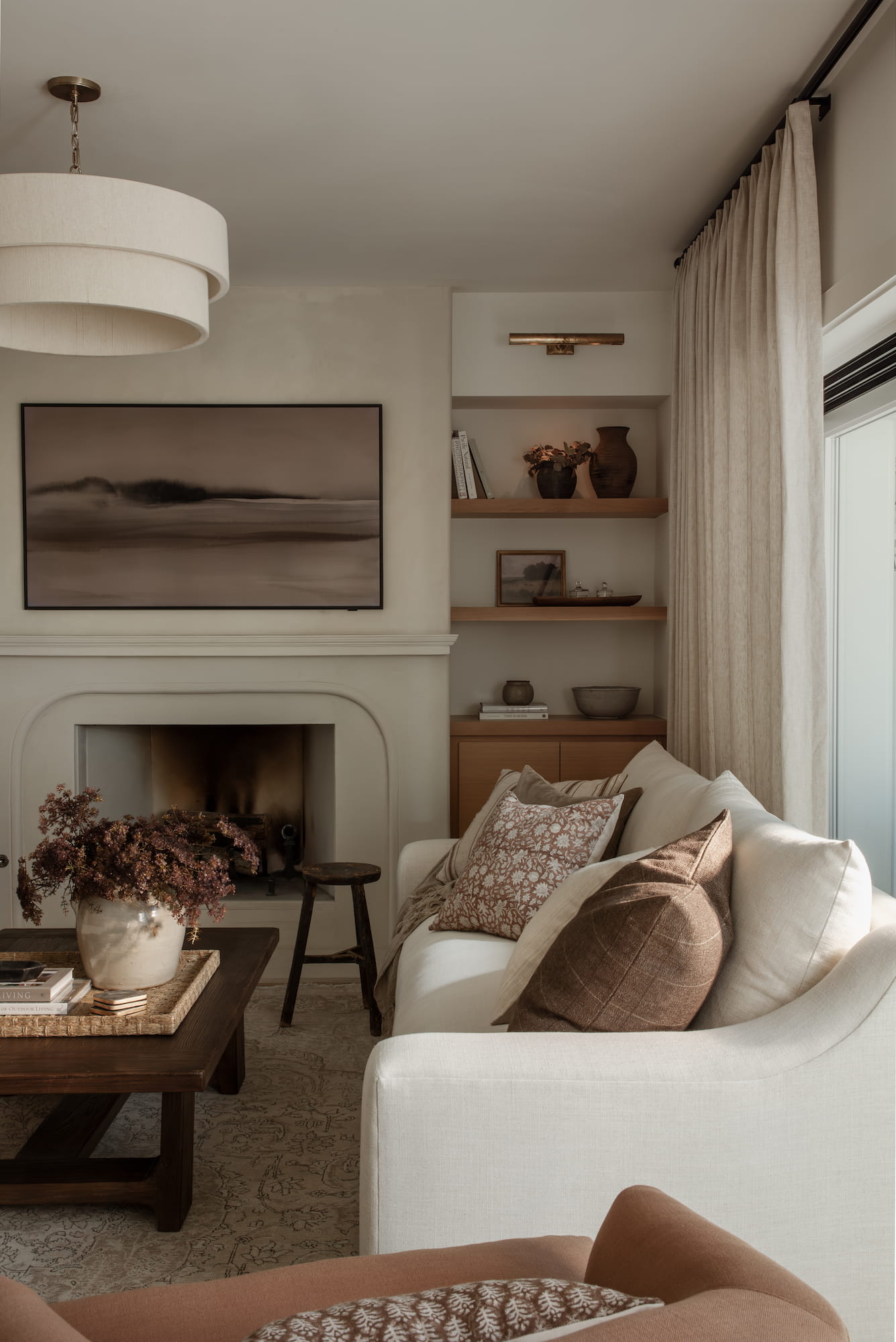 Living room with plaster fireplace, oak built-in shelving, and layered neutral textiles in the Bellevue project, La Jolla, California — Joey Snow Design Co.