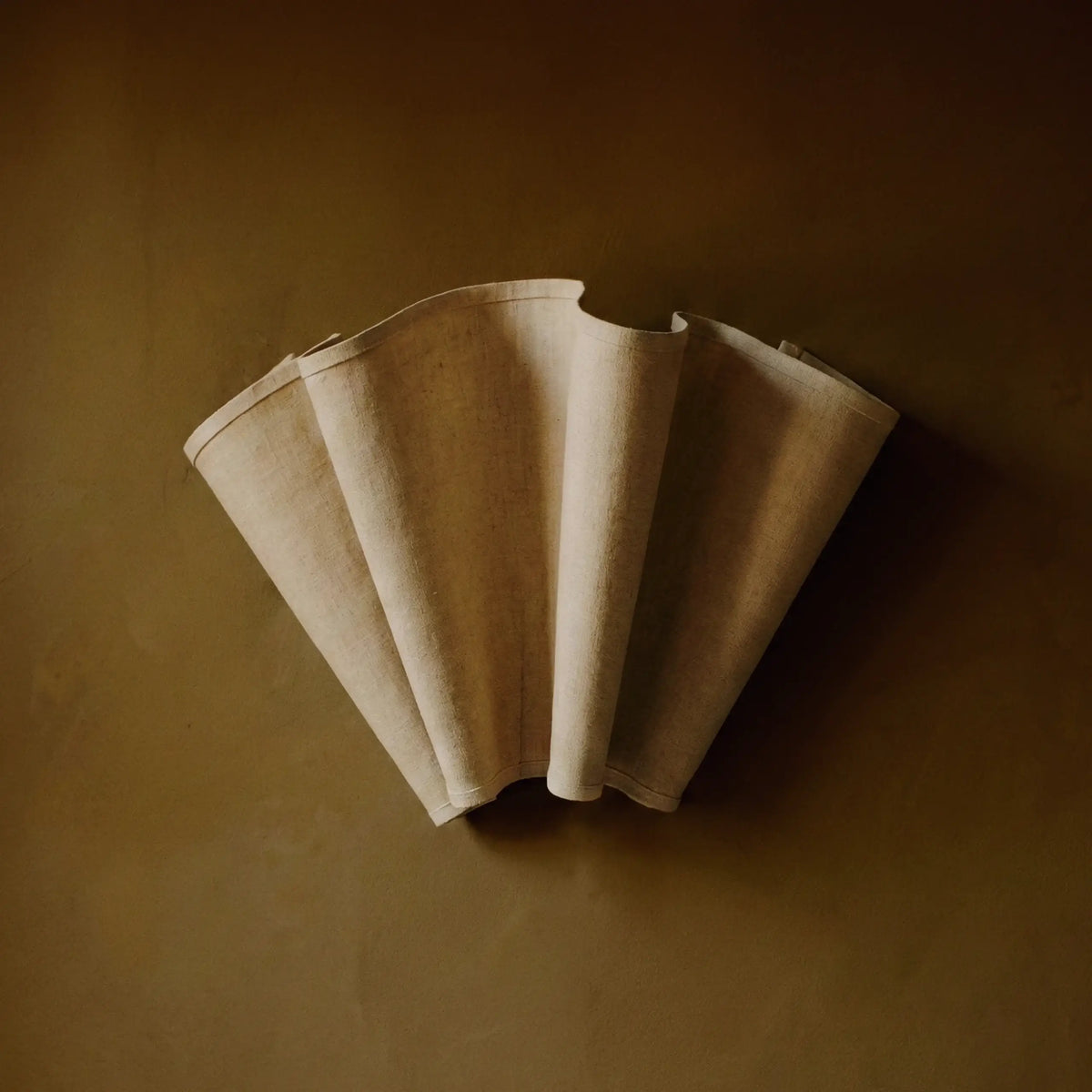 The Feuillet fluted wall sconce with a natural linen-texture fan shade, mounted on a warm brown wall
