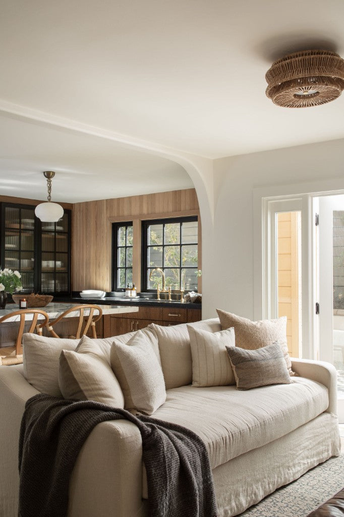 Living room with linen sofa and wood-paneled wet bar with black casement windows, designed by Joey Snow Design Co.