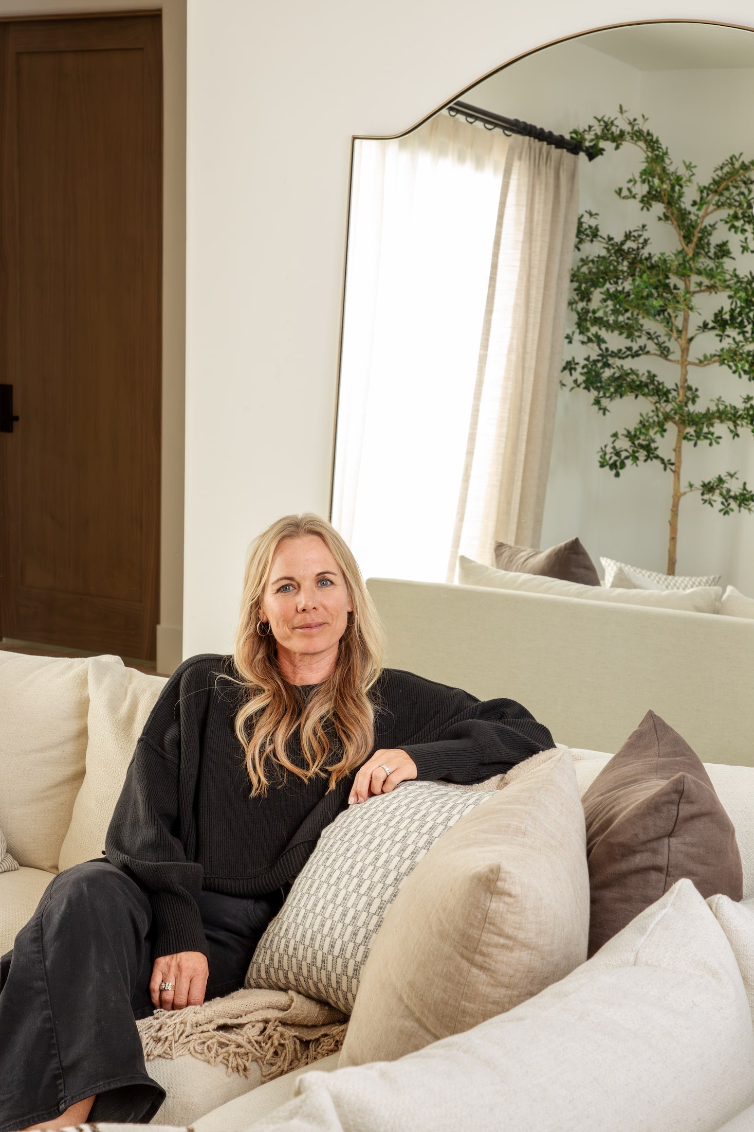 Interior designer Joey Snow seated in a light, neutral living room she designed, showcasing her studio’s warm and organic aesthetic.