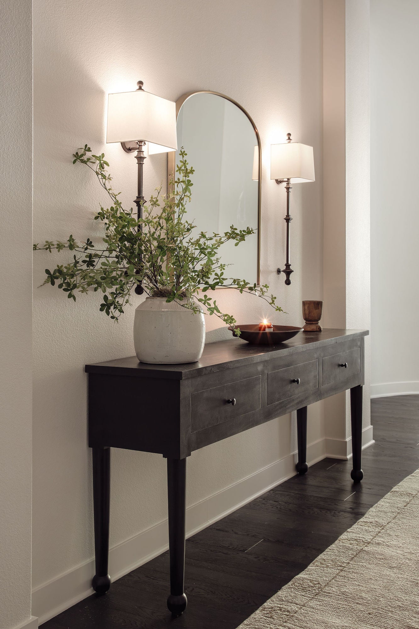 Dark wood console with arched brass mirror, twin linen sconces, and stoneware vase in the San Juan Spanish project, San Juan Capistrano, California — Joey Snow Design Co.