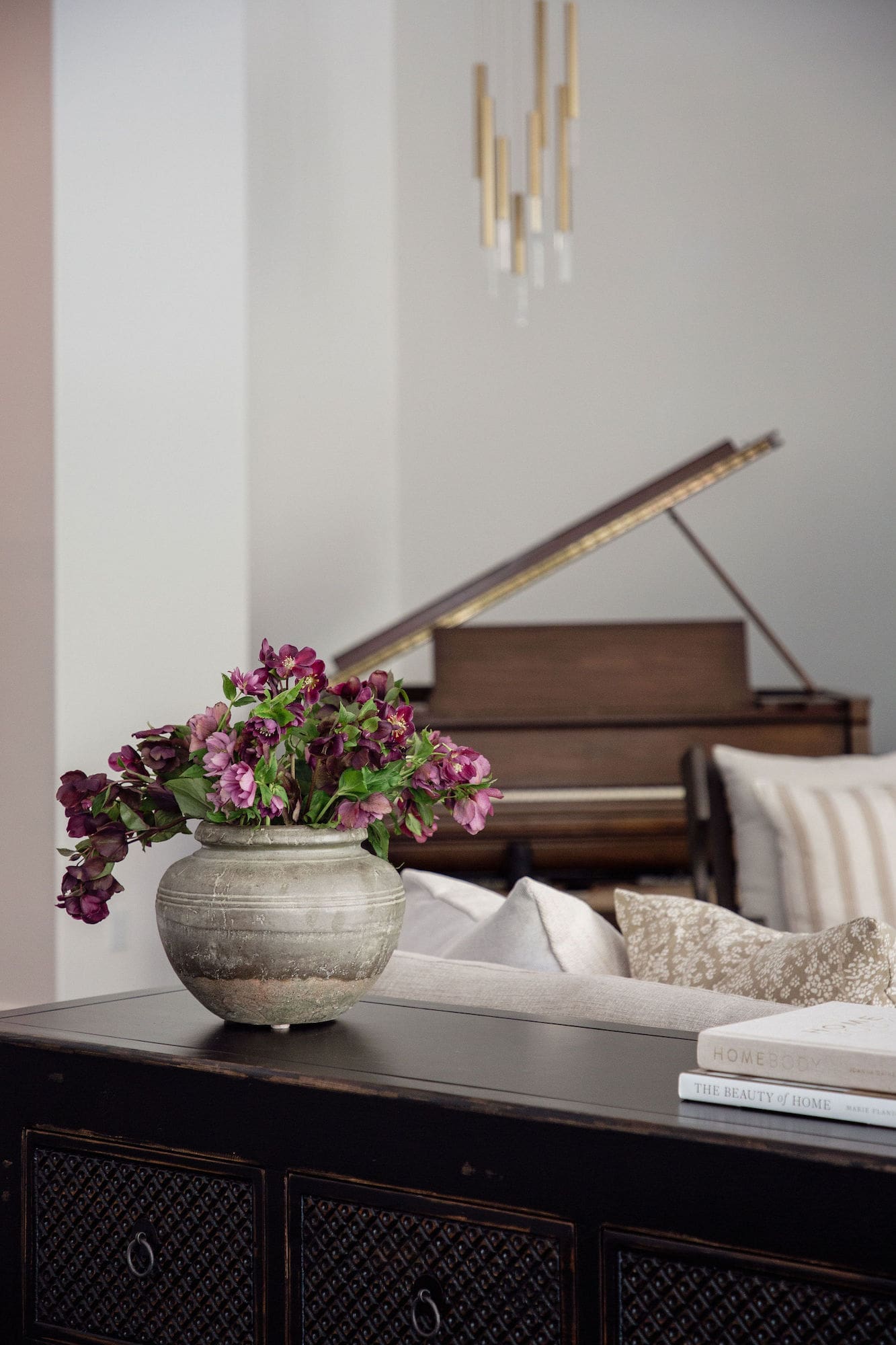 Aged clay pot of plum florals on a distressed black sideboard with grand piano beyond in the San Juan Spanish project, San Juan Capistrano, California — Joey Snow Design Co.