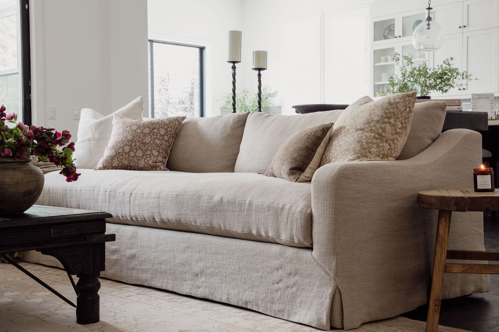 Slipcovered linen sofa layered with block-print pillows beside an antique black coffee table in the San Juan Spanish project, San Juan Capistrano, California — Joey Snow Design Co.