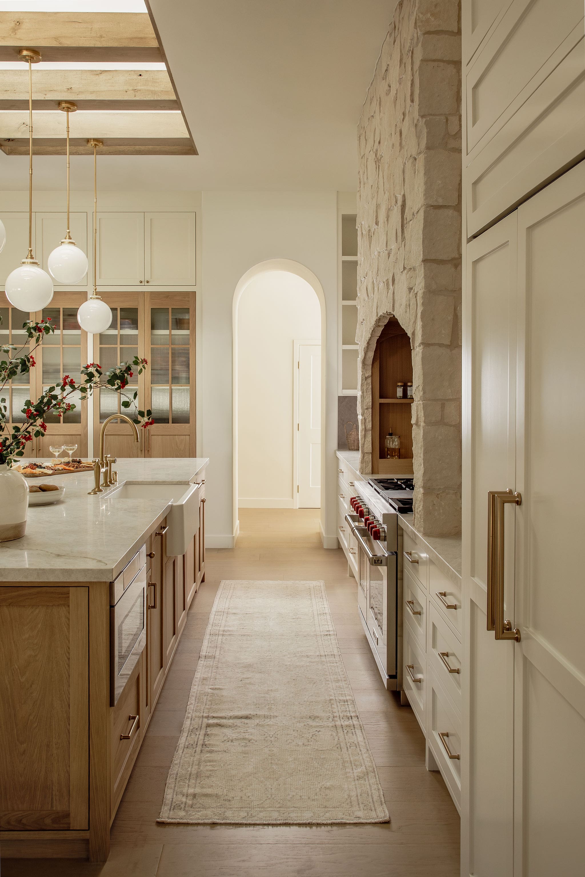 Galley kitchen view with long island, light wood cabinetry, brass hardware, and neutral runner rug.